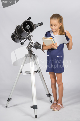 Image of Schoolgirl leafing through a textbook while standing at the telescope