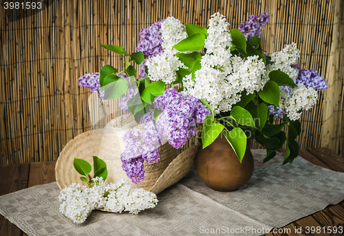 Image of Still-life with a bouquet of lilacs and a straw hat, close-up