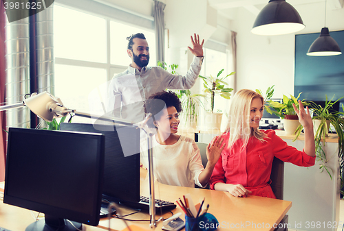 Image of happy creative team waving hands in office