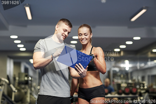 Image of smiling young woman with personal trainer in gym