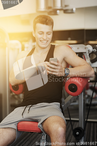 Image of smiling young man with smartphone in gym