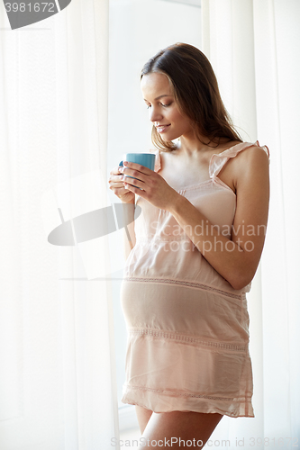 Image of happy pregnant woman with cup drinking tea at home