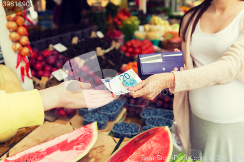 Image of pregnant woman with wallet buying food at market