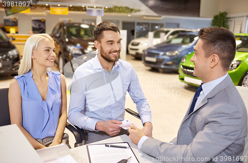 Image of happy couple with car dealer in auto show or salon