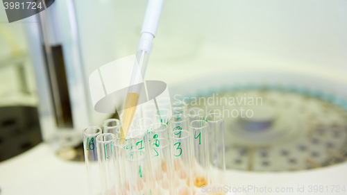 Image of pipette dropping sample into a test tube,abstract science background