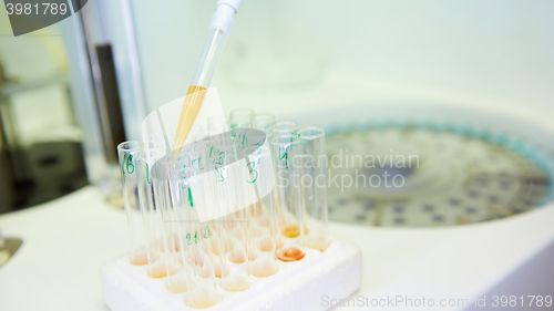 Image of pipette dropping sample into a test tube,abstract science background