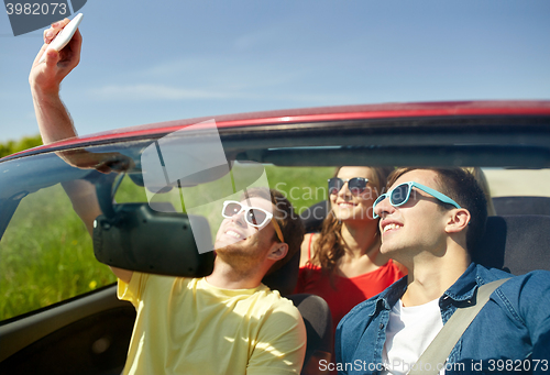 Image of friends driving in cabriolet car and taking selfie