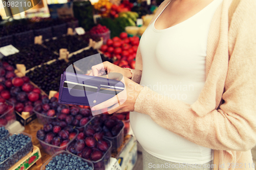 Image of pregnant woman with wallet buying food at market