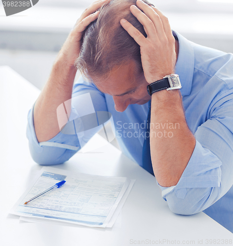 Image of stressed businessman with papers at work