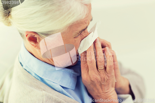 Image of sick senior woman blowing nose to paper napkin