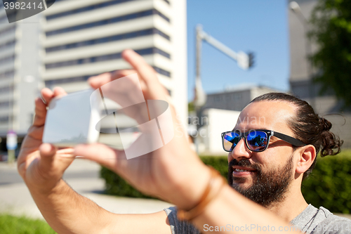 Image of man taking video or selfie by smartphone in city