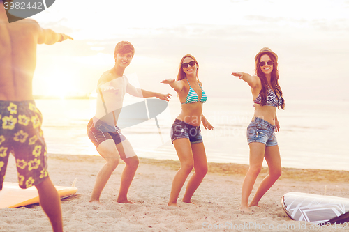 Image of smiling friends in sunglasses with surfs on beach