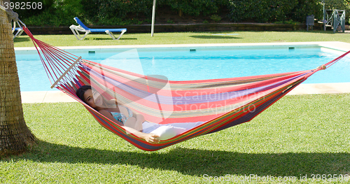 Image of Woman in hammock at tropic resort with pool