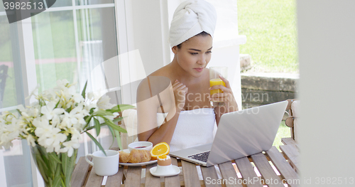 Image of Woman in towel with laptop having breakfast