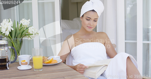 Image of Woman in bath towel reading book at table