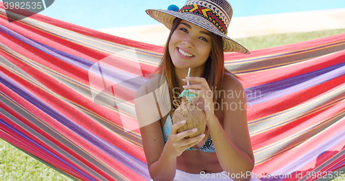 Image of Woman with coconut drink and sitting in hammock