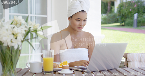 Image of Young woman using a laptop while having breakfast