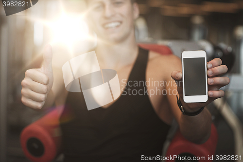 Image of young man with smartphone showing thumbs up in gym