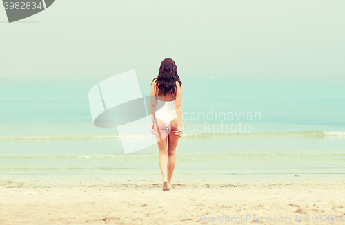 Image of young woman in swimsuit walking on beach