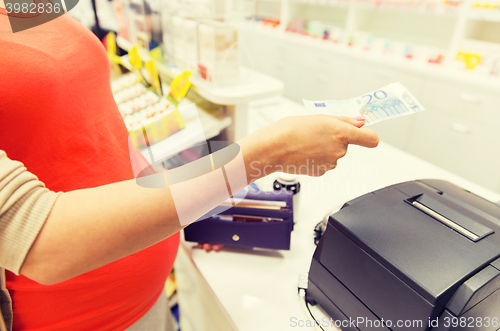 Image of pregnant woman with money at cashbox in drugstore