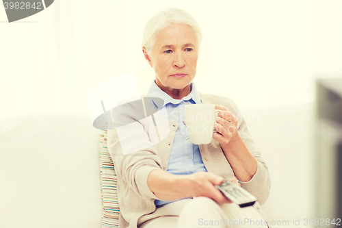 Image of senior woman watching tv and drinking tea at home