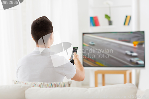 Image of man with remote watching motorsports on tv at home