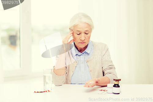 Image of senior woman with water and medicine at home