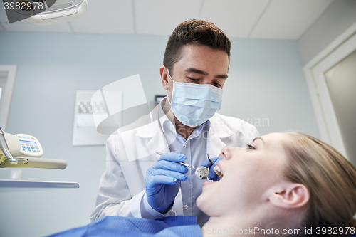 Image of male dentist in mask checking female patient teeth