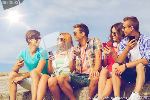 Image of group of smiling friends with smartphones outdoors