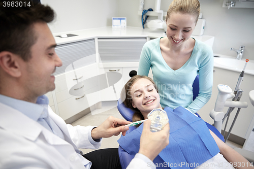 Image of happy dentist showing toothbrush to patient girl