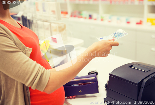 Image of pregnant woman with money at cashbox in drugstore