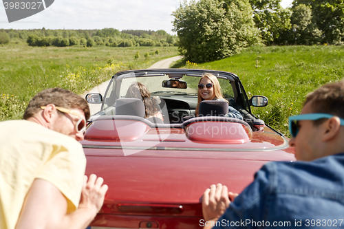 Image of happy friends pushing broken cabriolet car