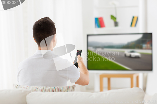 Image of man with remote watching motorsports on tv at home