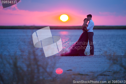 Image of Young romantic couple relaxing on the beach watching the sunset
