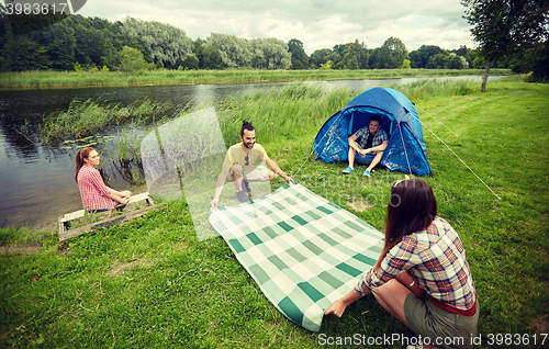 Image of happy friends laying picnic blanket at campsite