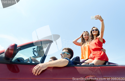 Image of friends driving in cabriolet car and taking selfie