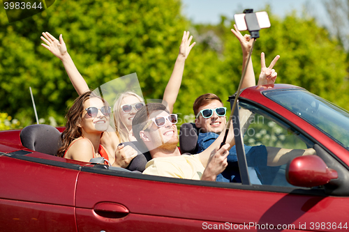 Image of friends driving in cabriolet car and taking selfie