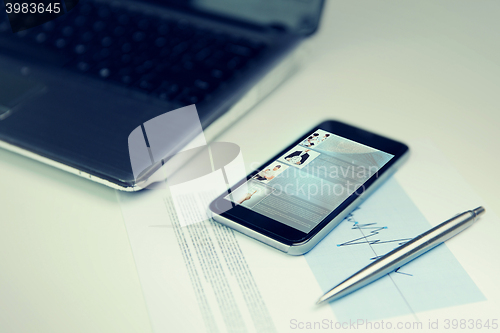 Image of close up of smartphone, laptop and pen on table