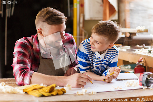 Image of happy father and son with blueprint at workshop