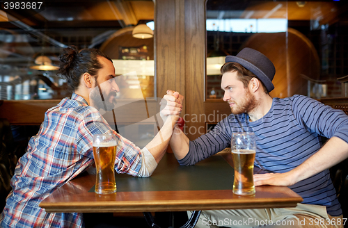 Image of men drinking beer and arm wrestling at bar or pub