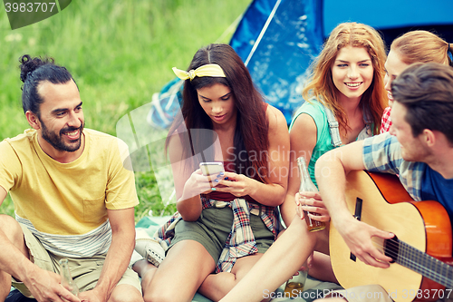 Image of happy friends with drinks and guitar at camping