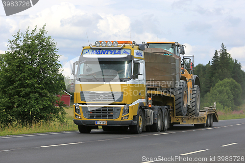 Image of Volvo FH16 Semi Hauls Wheel Loader Through Rural Scenery