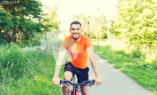 Image of happy young man riding bicycle outdoors