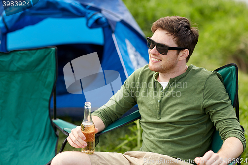 Image of happy young man drinking beer at campsite tent