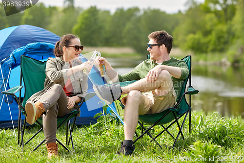 Image of happy couple clinking drinks at campsite tent