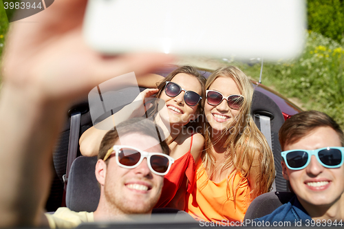 Image of friends driving in cabriolet car and taking selfie