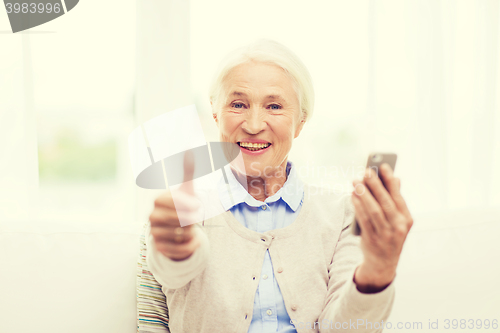 Image of senior woman with smartphone showing thumbs up