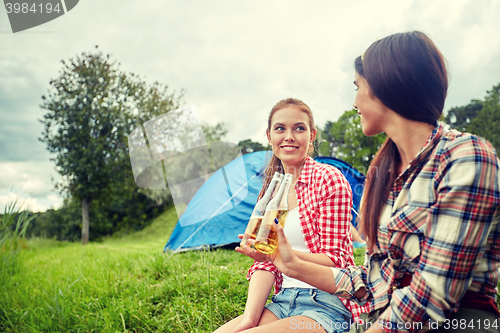 Image of happy young women with tent and drinks at campsite