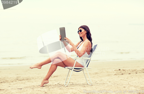 Image of smiling woman with tablet pc sunbathing on beach