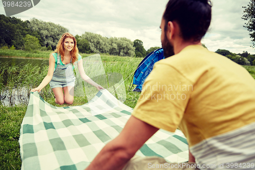 Image of happy couple laying picnic blanket at campsite